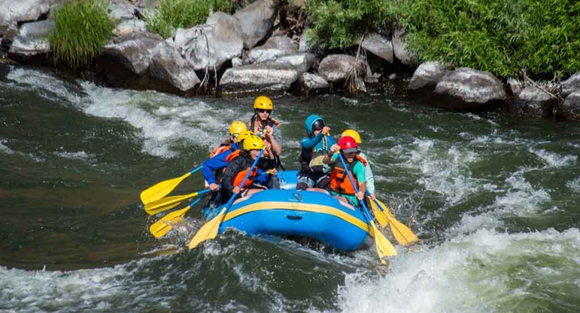 a group of high school students navigate whitewater in a raft
